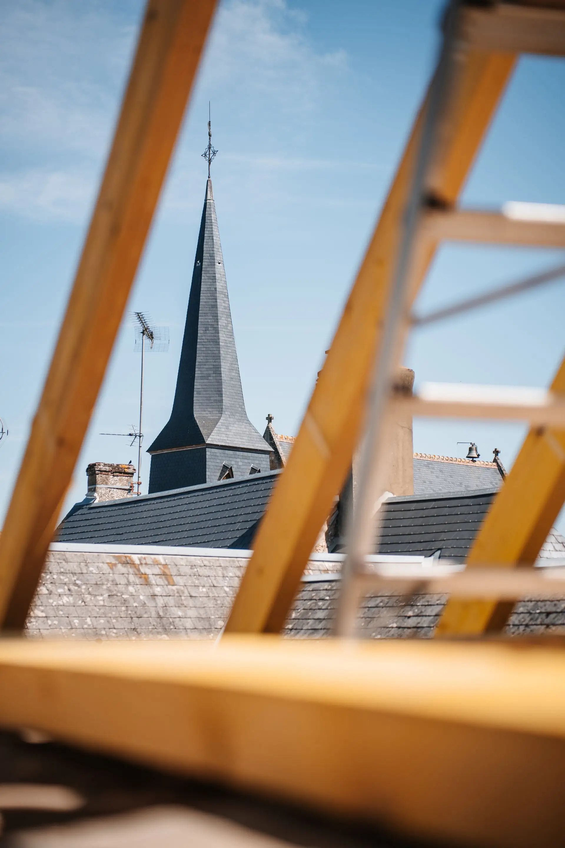Charpente en bois neuve avec vue sur un clocher depuis le chantier
