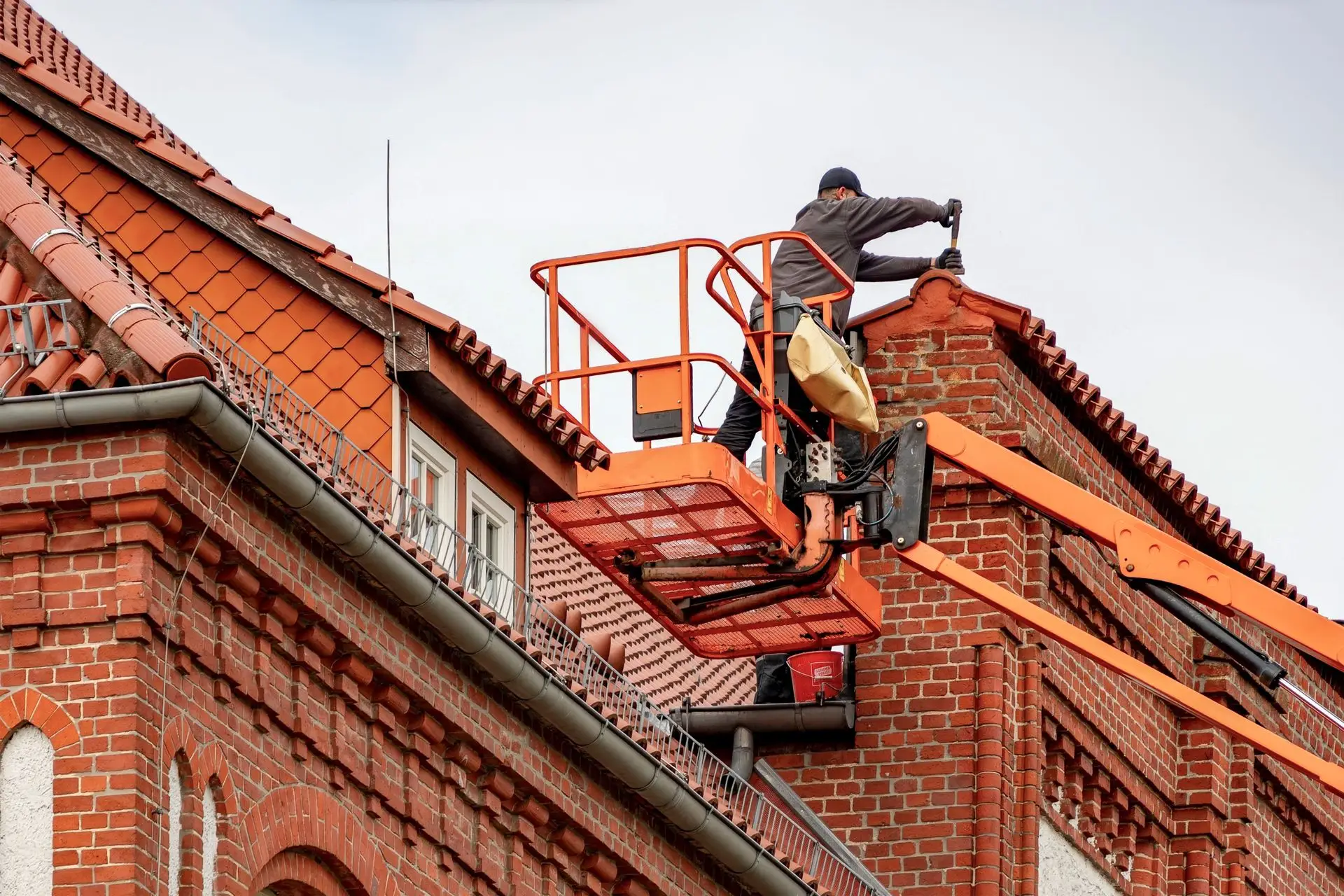 Couvreur en nacelle réparant une toiture en tuiles et sa gouttière sur un bâtiment en briques