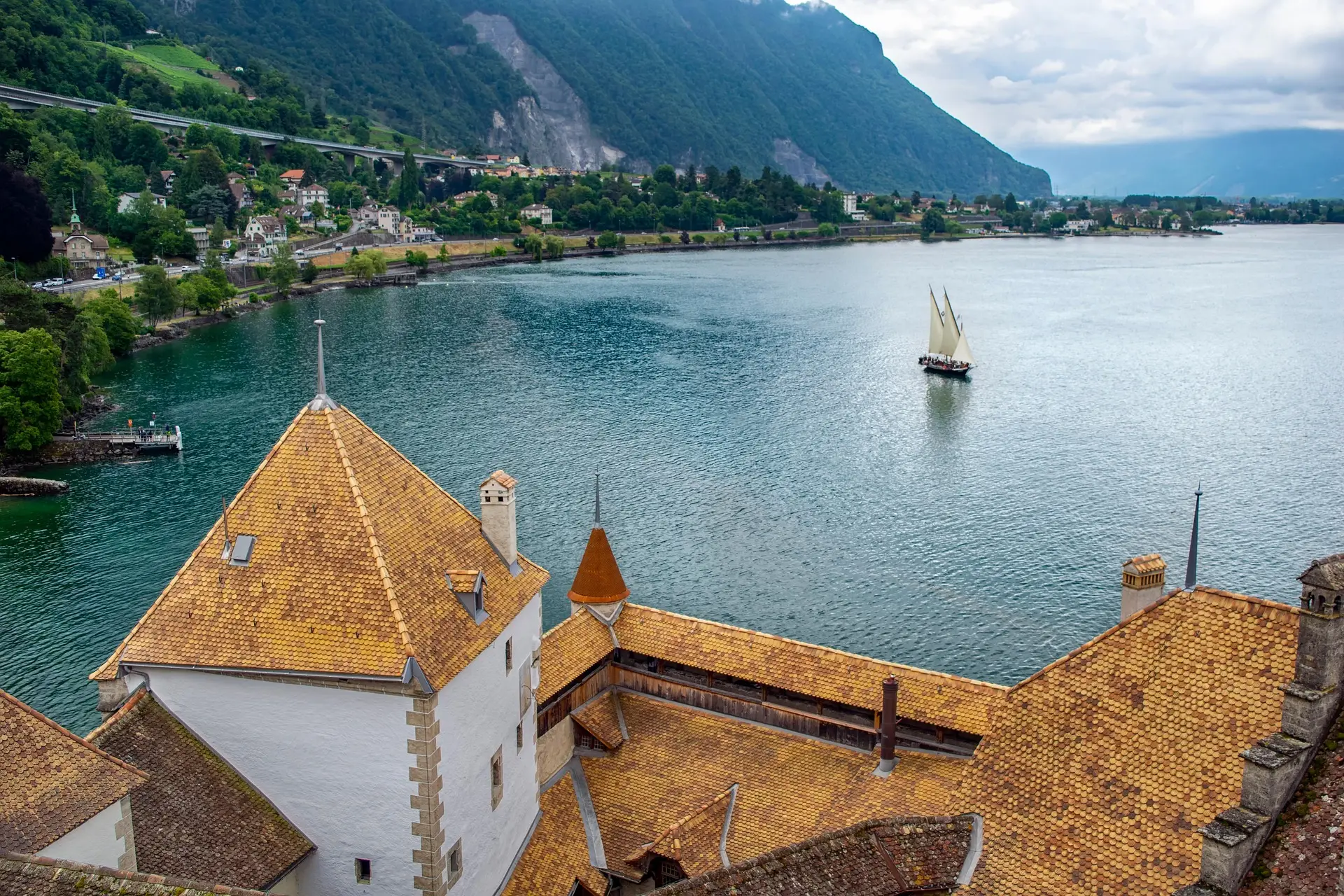 Toitures en tuiles ocre d’un bâtiment au bord d’un lac face à la montagne